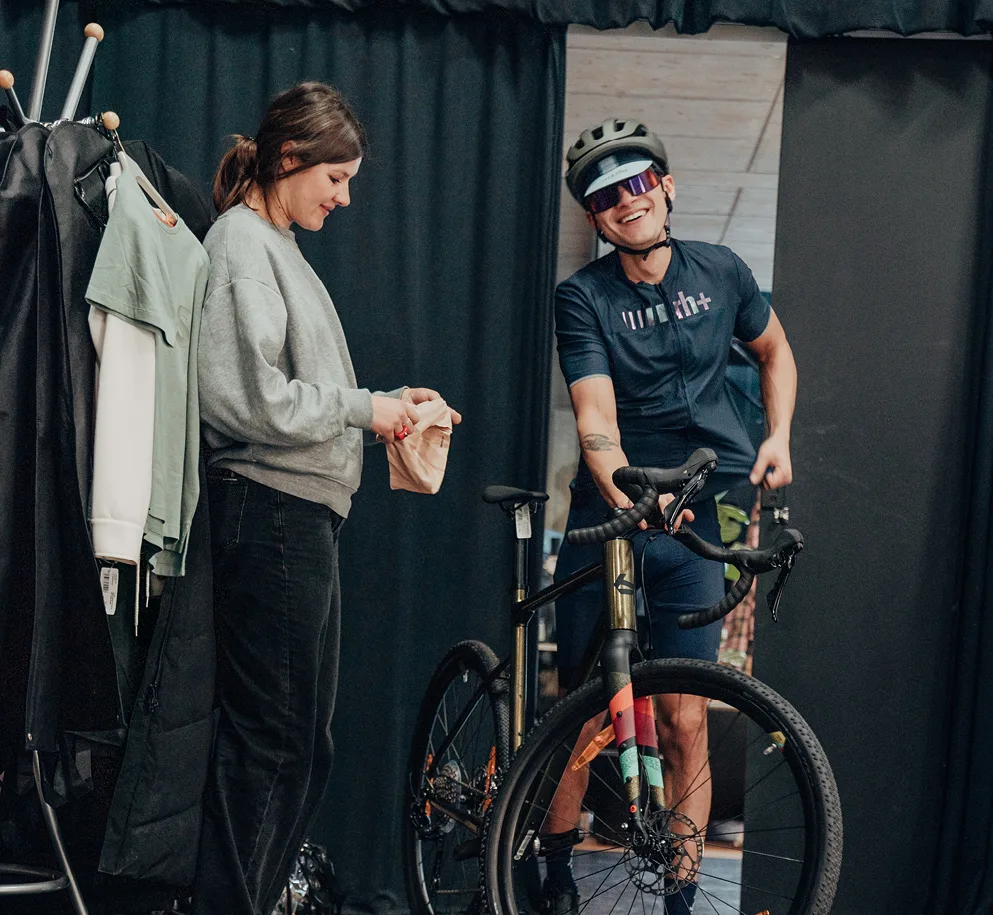 Fotografie aufgenommen während eines Fotoshootings für Reischmann. Auf dem Bild ist eine Mitarbeiterin des Teams zu sehen, die neben einem der Fahrradmodelle lächelt. Der Model hält ein Fahrrad und lacht