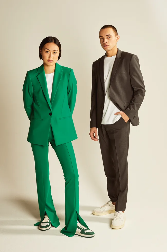 Zwei Models posieren für ein Reischmann-Fotoshooting und tragen jeweils einen zweiteiligen Anzug. Die Frau trägt einen grünen Anzug und der Mann trägt einen schwarzen Anzug