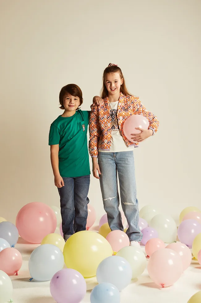 Zwei Kindermodels posieren bei einem Fotoshooting für Reischmann auf einem Boden voller bunter Luftballons