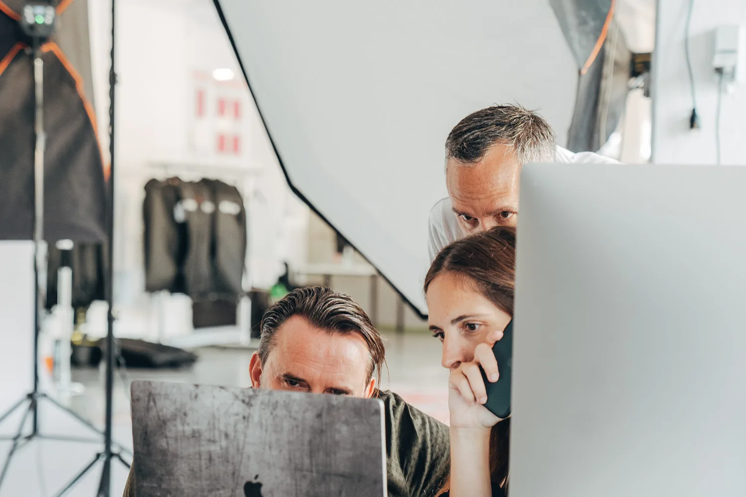 3 Personen hinter 2 Bildschirmen schauen sich Bilder an. Im Hintergrund Fotoshooting Equipment