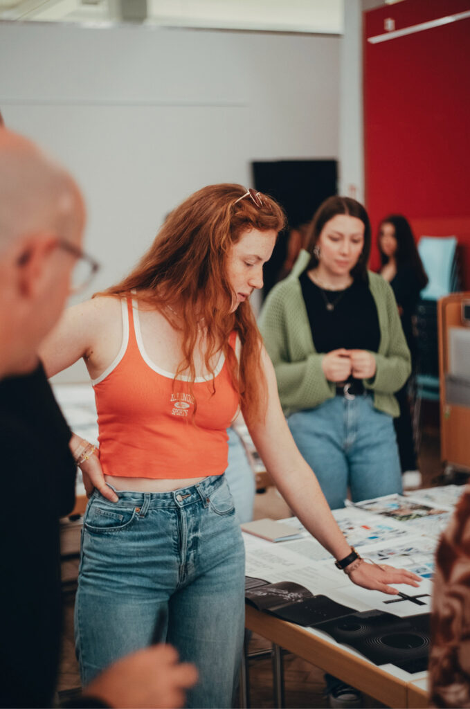 Junge Frau präsentiert Designentwürfe und diskutiert mit Teammitgliedern über kreative Konzepte. Teamwork und visuelle Gestaltung im Fokus.