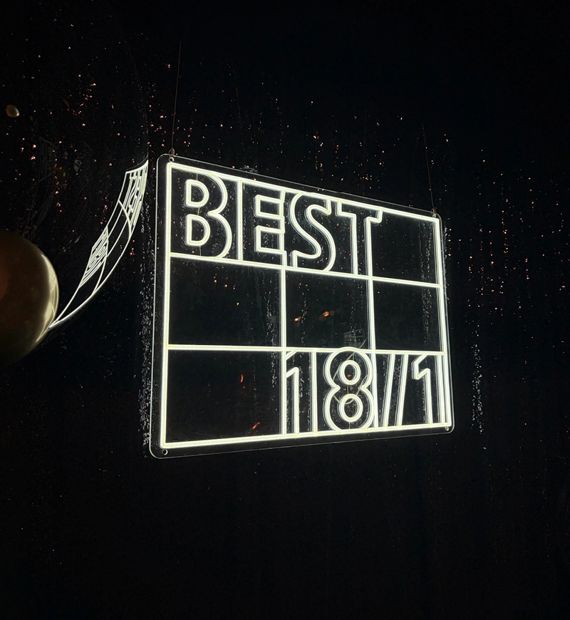 Neonreklame vor dunklem Hintergrund, auf der in der oberen Zeile „BEST“ und in der unteren Zeile „18/1“ zu lesen ist, im Hintergrund sind Wassertropfen zu sehen.