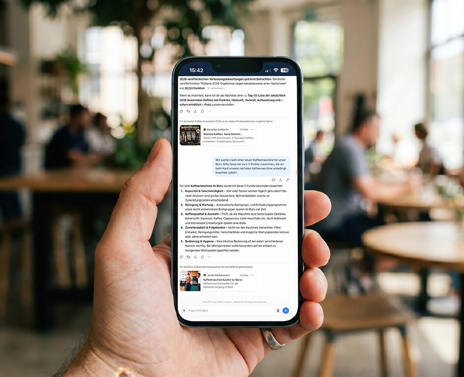 Eine Person hält in einem hellen, modernen Café ein Smartphone in der Hand, auf dessen Bildschirm eine Messaging-App zu sehen ist; im Hintergrund sitzen verschwommene Menschen an Tischen, was die Atmosphäre einer dynamischen Social-Media-Kampagne perfekt einfängt.